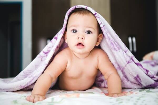 baby propping themselves up with their arms with a blanket over their head and shoulders